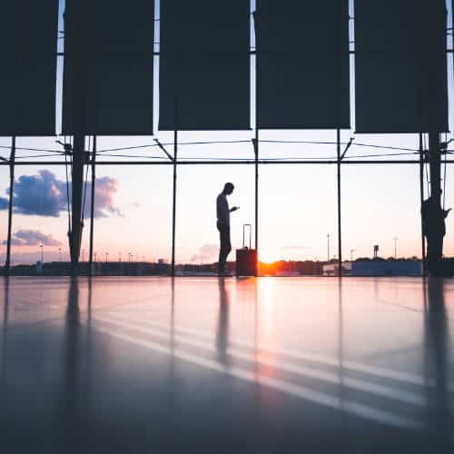 A lone passenger silhouetted against a large terminal window in low light