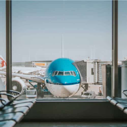 A turquoise airliner parked at a terminal gate, seen through the terminal windows