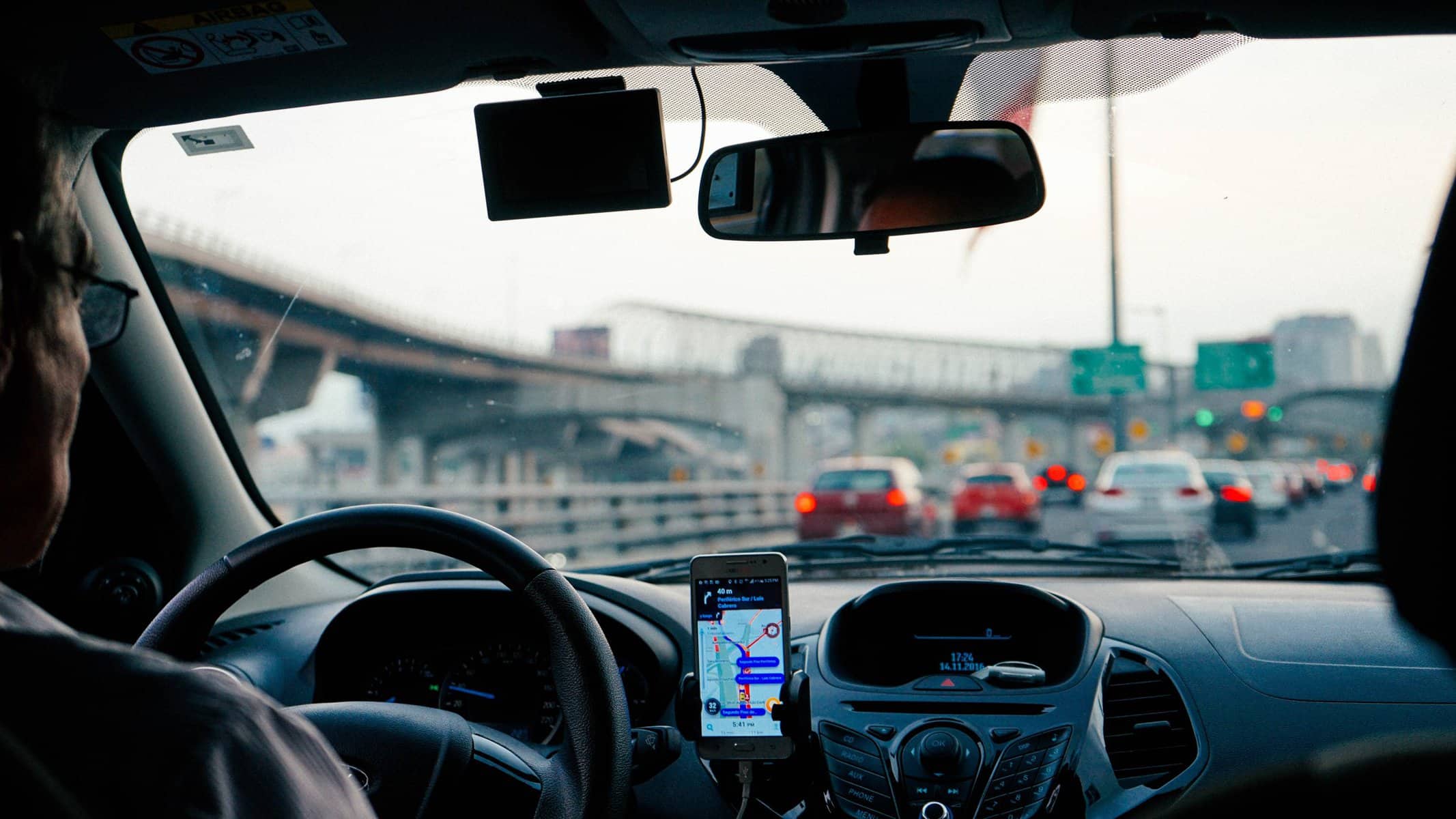 View through a car windscreen of a busy road, with a phone showing directions on the dashboard