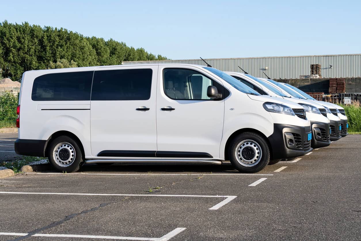 Row of white minibuses parked in a yard