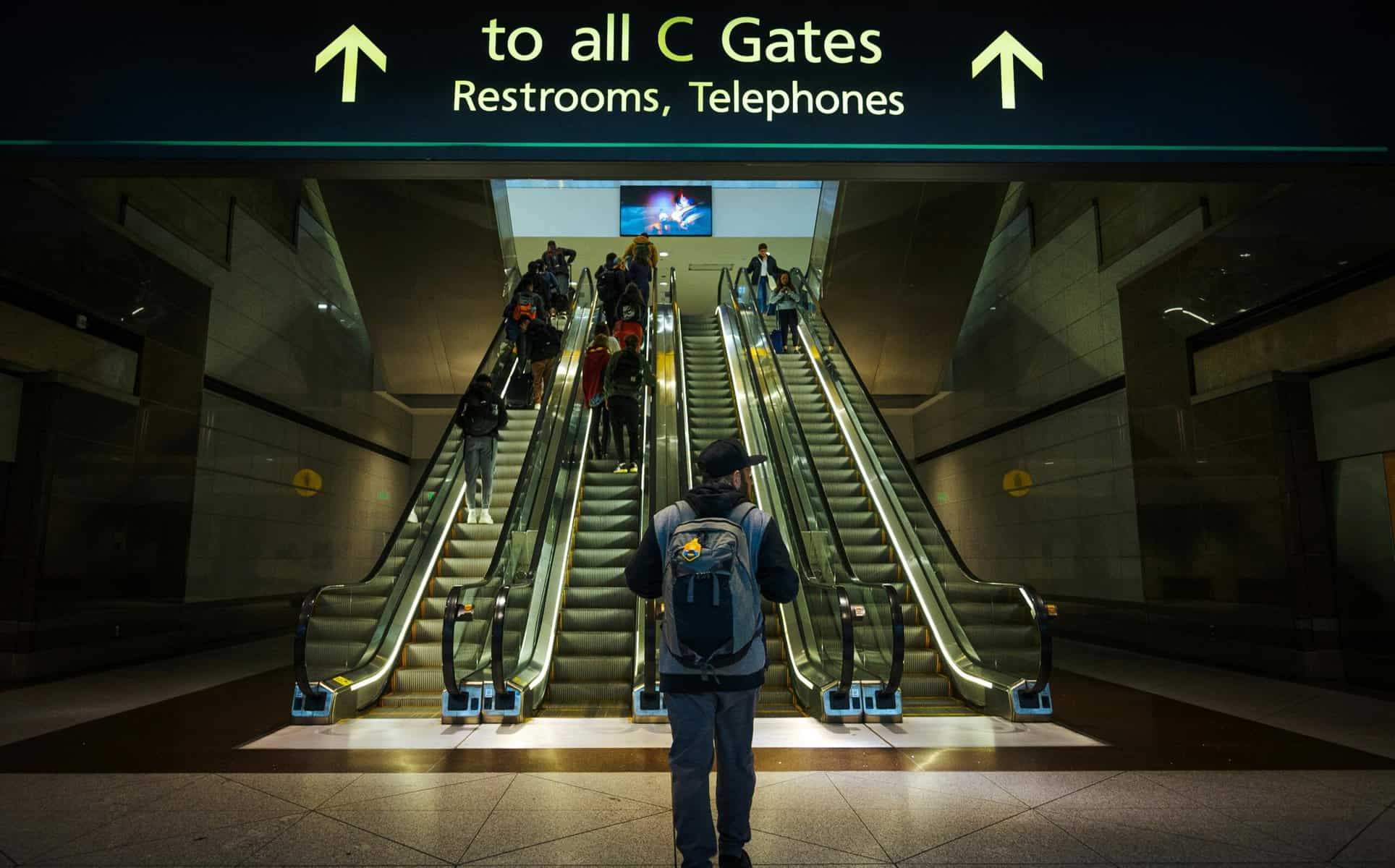 Airport terminal escalators beneath a gate direction sign