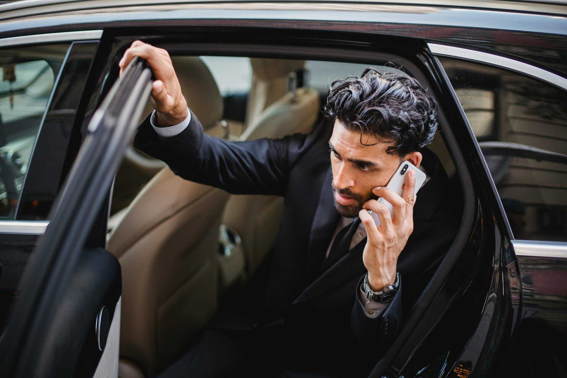 A man in a dark suit stepping out of a car while taking a phone call
