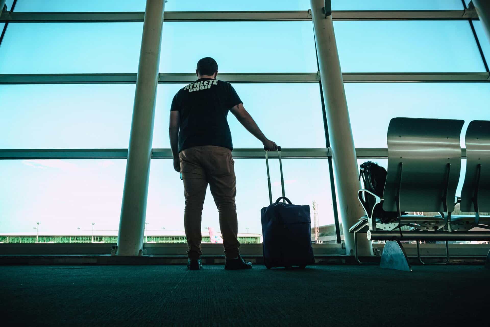A traveller with a suitcase standing at a tall terminal window with seats behind