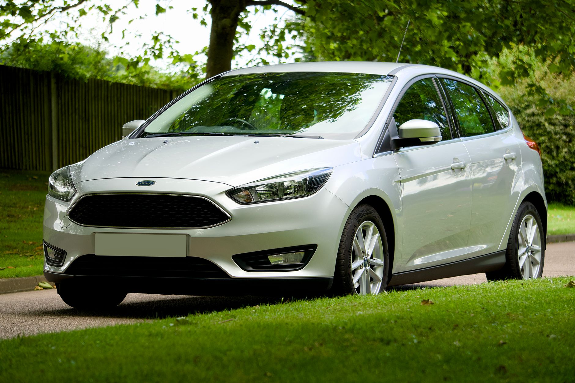 A silver Ford Focus hatchback parked on a leafy street during the day, showcasing its sleek design.