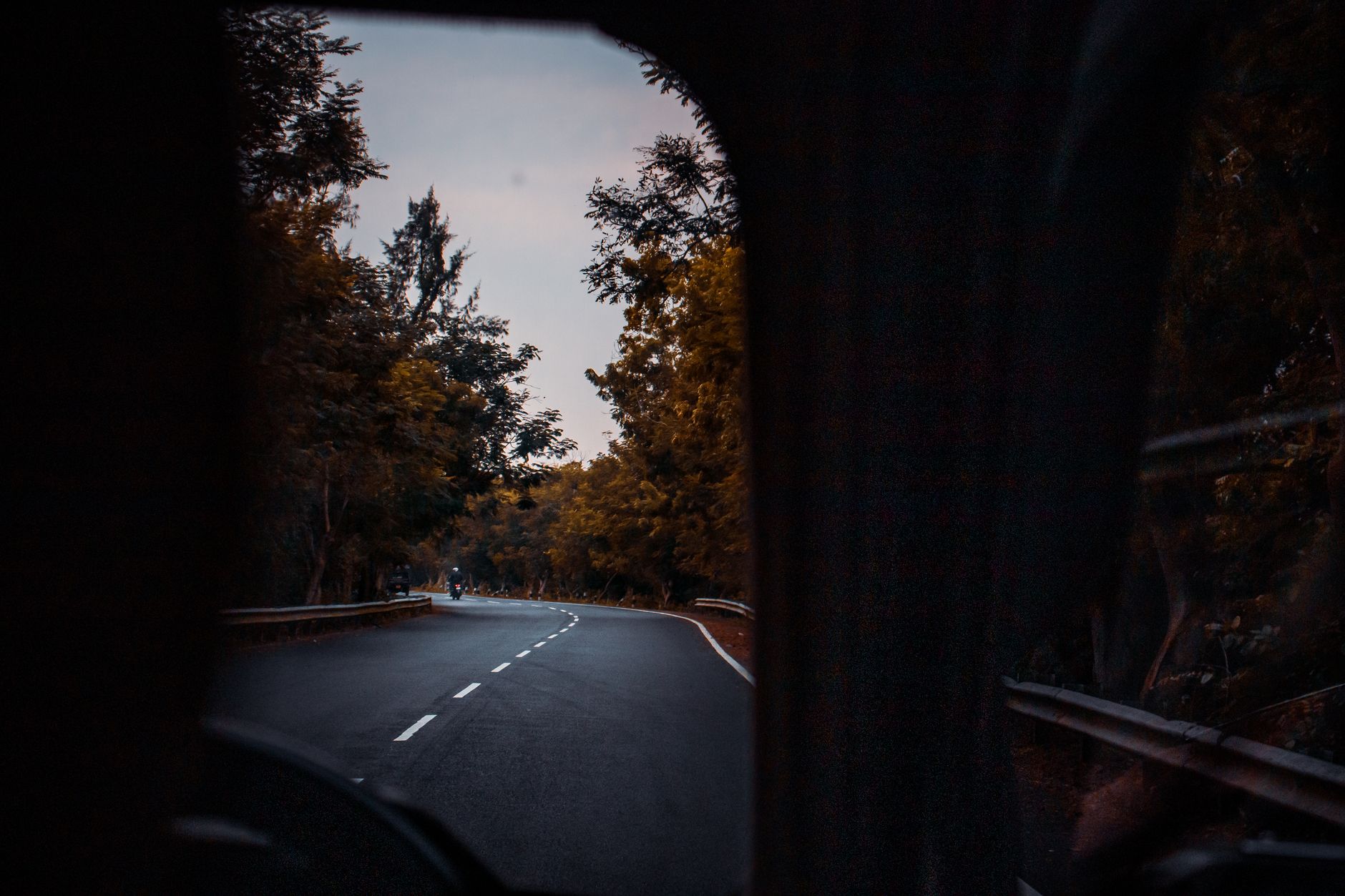 Through windshield glass of curvy asphalt road going through lush autumn forest against cloudy sunset sky