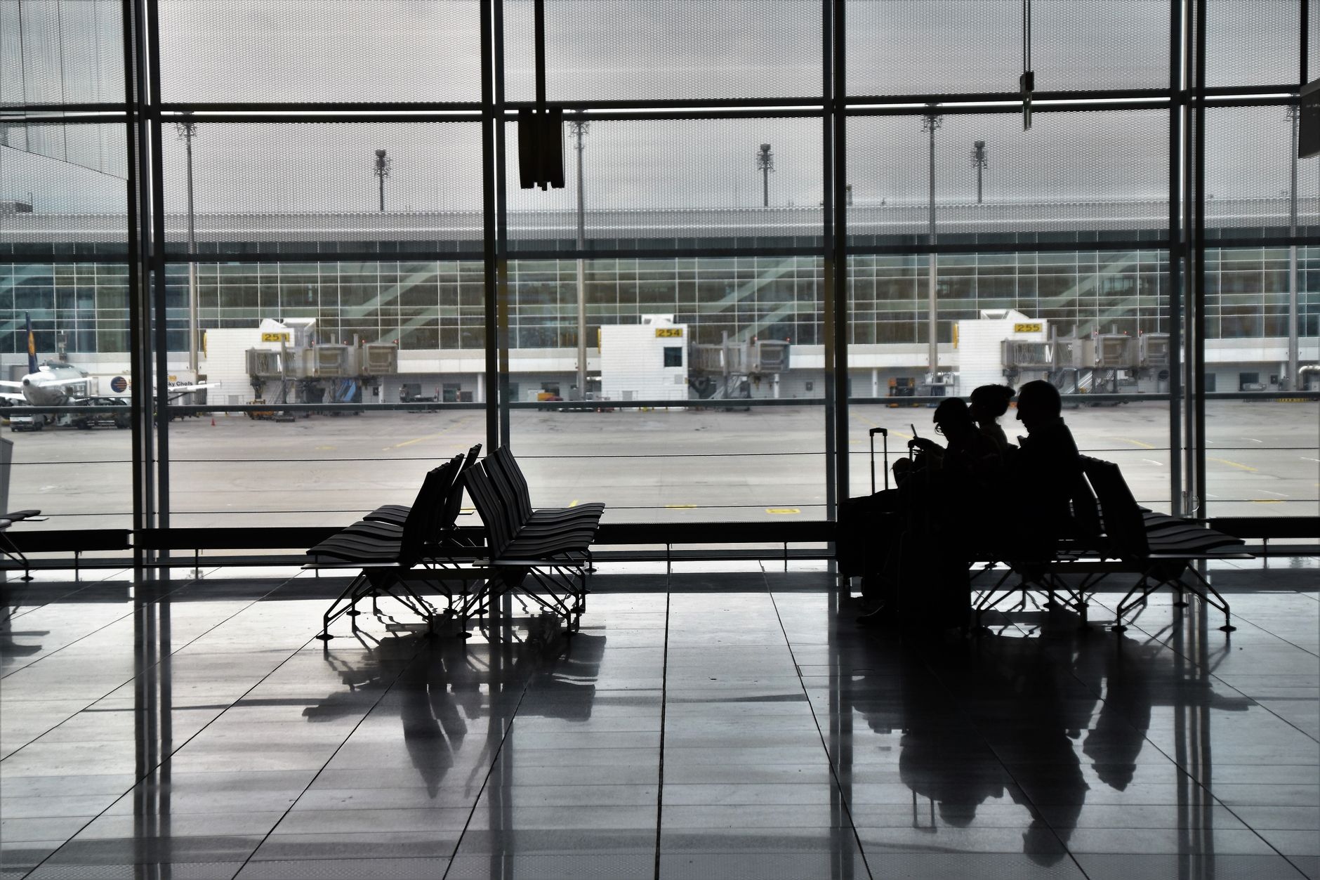 Silhouette of unrecognizable passengers sitting on chairs with luggage near  window and waiting for flight
